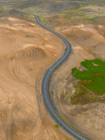 Aerial view of a winding road cuts through contrasting geothermal terrain a dance of ochre earth and verdant fields Reykjahl&iacute;&eth; &THORN;ingeyjarsveit Iceland.