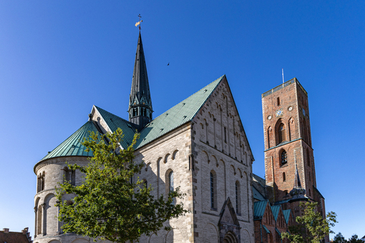 View of Ribe Cathedral featuring its Romanesque stone walls green copper roofs and the tall red brick Commoners Tower under a clear blue sky in Ribe Denmark. View of Ribe Cathedral featuring its Romanesque stone walls green copper roofs and the tall red brick Commoners Tower under a clear blue sky in Ribe Denmark.