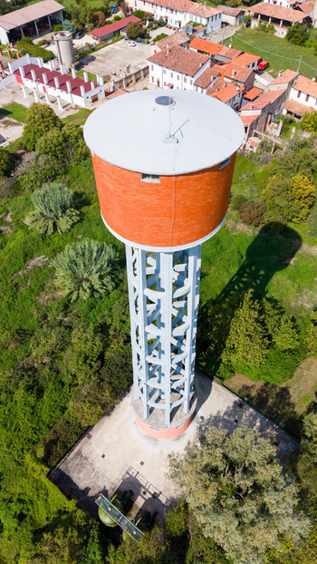 Aerial view of the water tower surrounded by lush green trees and nearby rural buildings in Mediglia Lombardy Italy.