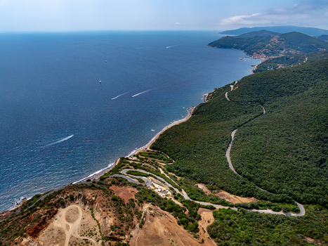 Aerial view of the old iron mine area near Laghetto delle conche featuring rugged geological formations winding coastal roads and the blue Tyrrhenian Sea in Rio Marina Toscana Italy.