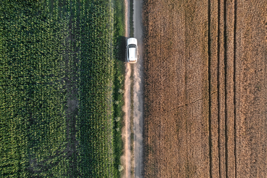 Aerial view of a lone white vehicle traverses a dusty path between verdant fields and sun scorched earth Chyhyrynskyi district Cherkasy Oblast Ukraine. Aerial view of a lone white vehicle traverses a dusty path between verdant fields and sun scorched earth Chyhyrynskyi district Cherkasy Oblast Ukraine.