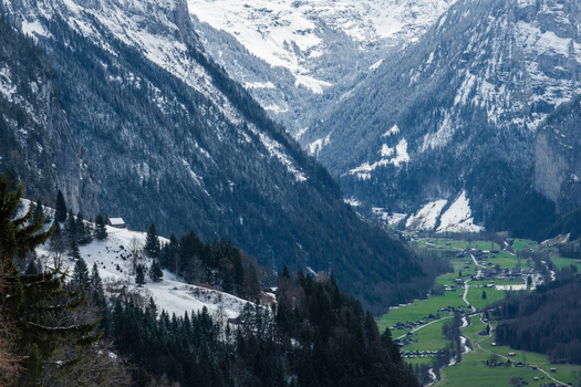 View of the deep valley with snow capped mountains and lush green meadows where small houses nestle peacefully alongside a winding river Wengen Switzerland. View of the deep valley with snow capped mountains and lush green meadows where small houses nestle peacefully alongside a winding river Wengen Switzerland.