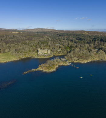 Aerial view of Dunvegan Castle and Gardens on a rocky promontory surrounded by dense woodland and the blue waters of Loch Dunvegan Isle of Skye Scotland United Kingdom. Aerial view of Dunvegan Castle and Gardens on a rocky promontory surrounded by dense woodland and the blue waters of Loch Dunvegan Isle of Skye Scotland United Kingdom.