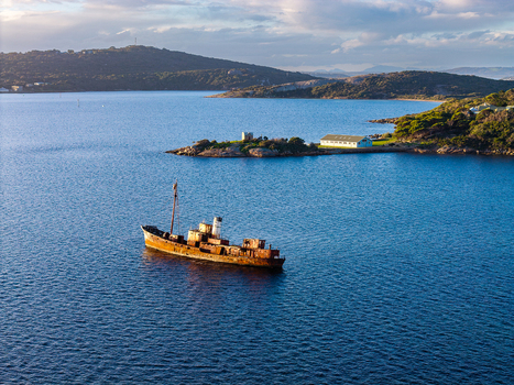 Aerial view of a rusty shipwreck at Camp Quaranup in the calm blue waters of the bay with coastal buildings on the shore Vancouver Peninsula Western Australia Australia. Aerial view of a rusty shipwreck at Camp Quaranup in the calm blue waters of the bay with coastal buildings on the shore Vancouver Peninsula Western Australia Australia.