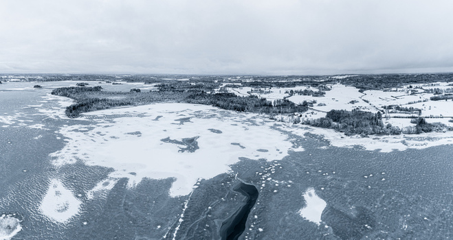 Aerial view of a frozen lake surrounded by snow covered forests and fields under a cloudy winter sky in Latvia. Aerial view of a frozen lake surrounded by snow covered forests and fields under a cloudy winter sky in Latvia.