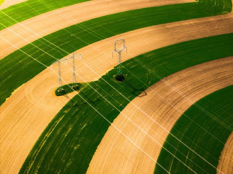 Aerial view of agricultural fields with alternating green and brown strips and high voltage power pylons casting long shadows in Brno South Moravian Region Czechia.