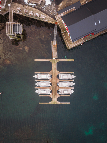 Aerial view of still boats docked at the pier reflecting in the water near the buildings Ballstad Nordland Norway. Aerial view of still boats docked at the pier reflecting in the water near the buildings Ballstad Nordland Norway.