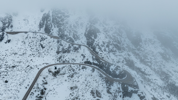 Aerial view of a winding mountain road snaking through the snow covered slopes and rocky terrain of the glacial valley under a thick fog in Loriga Guarda District Portugal. Aerial view of a winding mountain road snaking through the snow covered slopes and rocky terrain of the glacial valley under a thick fog in Loriga Guarda District Portugal.