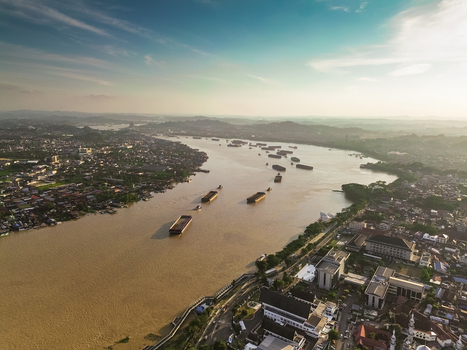 Aerial view of the Mahakam River with coal barges navigating through the urban landscape of Samarinda Kalimantan Timur Indonesia. Aerial view of the Mahakam River with coal barges navigating through the urban landscape of Samarinda Kalimantan Timur Indonesia.