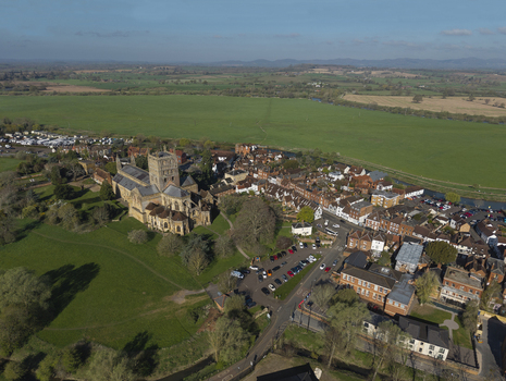 Aerial view of Tewkesbury Abbey surrounded by historic town buildings lush green fields and the river in Tewkesbury England United Kingdom.