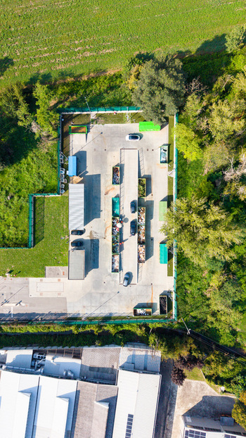 Aerial view of a recyclable waste collection point with various containers parked cars and concrete surfaces surrounded by green fields and trees in Bettola Zeloforamagno Lombardia Italy. Aerial view of a recyclable waste collection point with various containers parked cars and concrete surfaces surrounded by green fields and trees in Bettola Zeloforamagno Lombardia Italy.