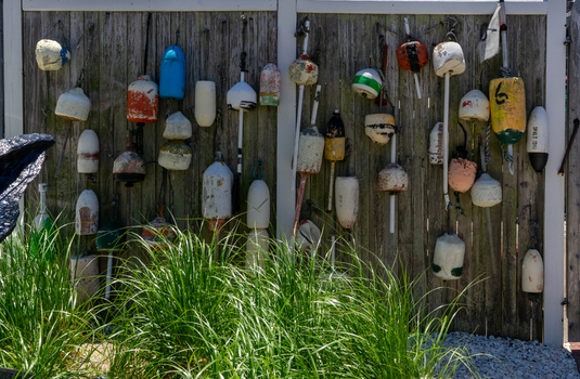 View of colorful weathered fishing buoys hanging on a rustic wooden fence with green grass in the foreground at Martha s Vineyard in Edgartown Massachusetts United States.