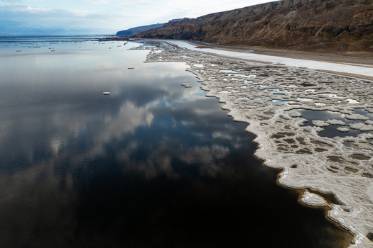 Aerial view of ice floes scattered across the dark reflective waters near a rugged shoreline contrasting sharply with the pale sky Israel. Aerial view of ice floes scattered across the dark reflective waters near a rugged shoreline contrasting sharply with the pale sky Israel.