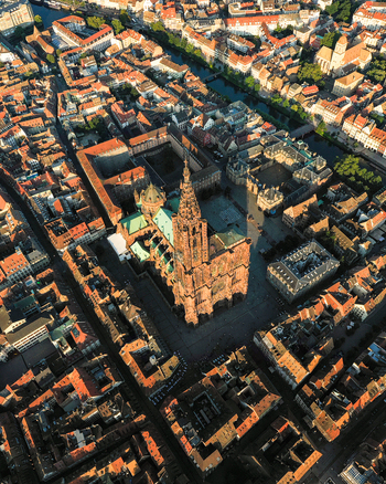 Aerial view of Cathedrale Notre Dame de Strasbourg surrounded by historic rooftops and urban architecture in the city center during golden hour in Strasbourg Grand Est France.