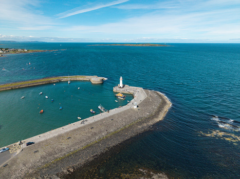 Aerial view of Donaghadee Harbour with its iconic lighthouse stone pier and small boats moored in the calm blue waters of the Irish Sea in Donaghadee Northern Ireland United Kingdom. Aerial view of Donaghadee Harbour with its iconic lighthouse stone pier and small boats moored in the calm blue waters of the Irish Sea in Donaghadee Northern Ireland United Kingdom.