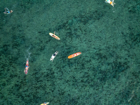 Aerial view of surfers paddling on colorful surfboards in the clear turquoise waters of Mahaybo Beach General Luna Caraga Philippines. Aerial view of surfers paddling on colorful surfboards in the clear turquoise waters of Mahaybo Beach General Luna Caraga Philippines.
