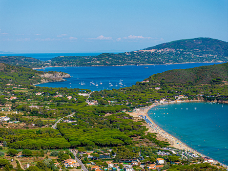 Aerial view of Lacona Beach with its sandy coastline turquoise waters anchored boats and surrounding lush pine forests in Lacona Tuscany Italy.