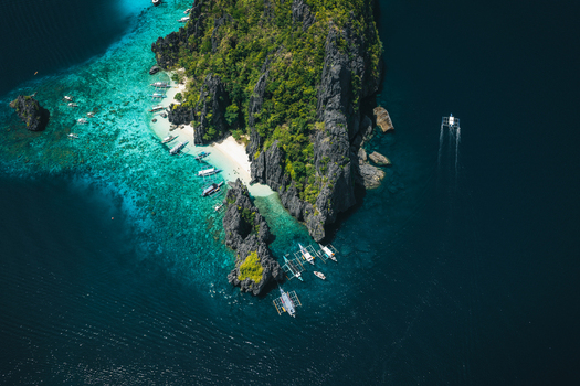 Aerial view of limestone cliffs turquoise waters and traditional outrigger boats anchored near a white sand beach in El Nido Mimaropa Philippines. Aerial view of limestone cliffs turquoise waters and traditional outrigger boats anchored near a white sand beach in El Nido Mimaropa Philippines.