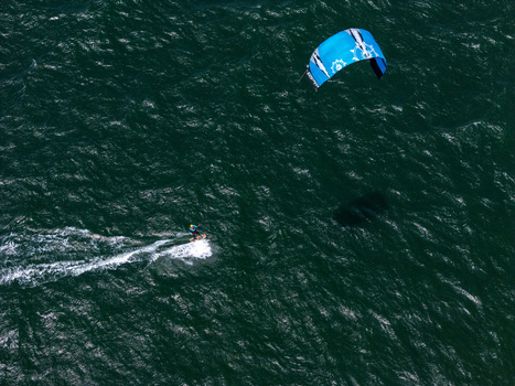 Aerial view of a kitesurfer gliding across the dark water with a blue kite at Depok Beach Special Region of Yogyakarta Indonesia. Aerial view of a kitesurfer gliding across the dark water with a blue kite at Depok Beach Special Region of Yogyakarta Indonesia.