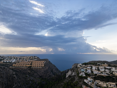 Aerial view of residential villas perched on rocky cliffs overlooking the Mediterranean Sea under a dramatic cloudy sky Moraira Valencian Community Spain.