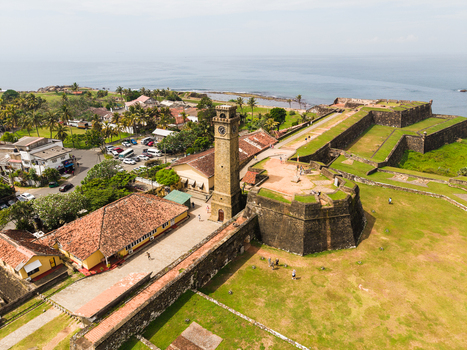 Aerial view of the historic Galle Fort Clock Tower and stone ramparts with people walking along the walls overlooking the Indian Ocean in Galle Southern Province Sri Lanka. Aerial view of the historic Galle Fort Clock Tower and stone ramparts with people walking along the walls overlooking the Indian Ocean in Galle Southern Province Sri Lanka.