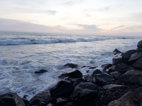 View of waves crashing against a rocky shoreline under a soft sunset sky Oceanside California United States. View of waves crashing against a rocky shoreline under a soft sunset sky Oceanside California United States.