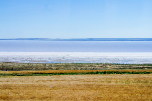View of the vast white salt flats and pinkish waters of Lake Tuz with golden fields in the foreground under a clear blue sky Ankara Ankara Turkiye. View of the vast white salt flats and pinkish waters of Lake Tuz with golden fields in the foreground under a clear blue sky Ankara Ankara Turkiye.
