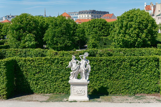 View of a classical white marble statue in the manicured gardens of Belvedere Palace with lush green hedges and city buildings under a clear blue sky Vienna Austria. View of a classical white marble statue in the manicured gardens of Belvedere Palace with lush green hedges and city buildings under a clear blue sky Vienna Austria.