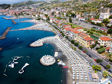 Aerial view of the vibrant coastline with rows of white beach umbrellas turquoise water and colorful buildings along the shore in San Lorenzo Liguria Italy.