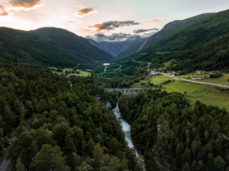 View of Kylling Bridge spanning the Rauma River in a lush valley surrounded by dense forests and mountains under a golden sunset sky in Rauma Municipality More og Romsdal Norway. View of Kylling Bridge spanning the Rauma River in a lush valley surrounded by dense forests and mountains under a golden sunset sky in Rauma Municipality More og Romsdal Norway.