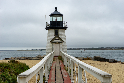 View of Brant Point Lighthouse with its wooden walkway leading to the entrance set against a sandy beach and the ocean under an overcast sky in Nantucket Massachusetts United States.