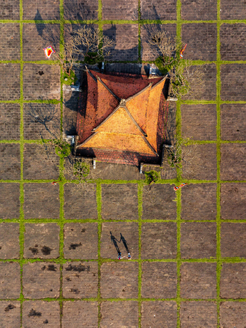Aerial view of a traditional pavilion with an orange tiled roof set in a stone grid courtyard with grass with two people holding hands casting long shadows in Vietnam. Aerial view of a traditional pavilion with an orange tiled roof set in a stone grid courtyard with grass with two people holding hands casting long shadows in Vietnam.