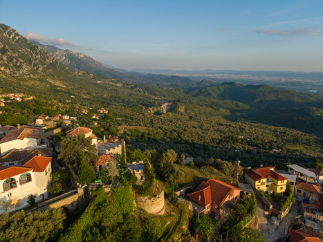 Aerial view of the historic Kruja Castle and traditional red roofed houses nestled on a hillside with lush mountains in Kruje Durres County Albania.
