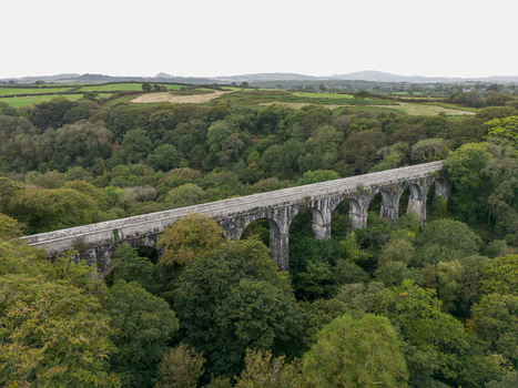 Aerial view of the historic stone Treffry Viaduct surrounded by dense woodland and rolling green hills in Luxulyan Cornwall United Kingdom.