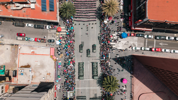 Aerial view of a military parade with soldiers and vehicles moving through a crowded city street lined with spectators and palm trees in Mexico City Mexico City Mexico.