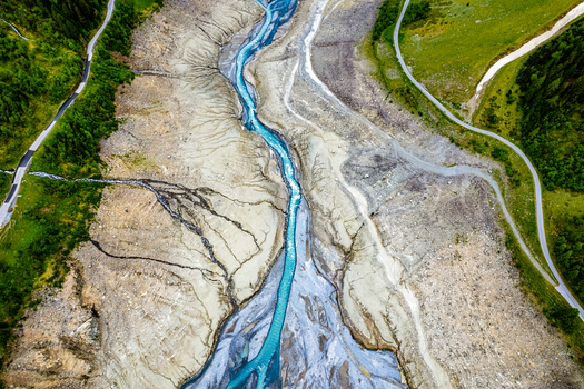 Aerial view of the turquoise glacial river flowing through a rocky valley bed with winding roads and lush green hillsides in Prutz Tyrol Austria. Aerial view of the turquoise glacial river flowing through a rocky valley bed with winding roads and lush green hillsides in Prutz Tyrol Austria.