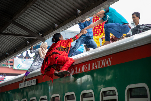 Dhaka Bangladesh 15 June 2018 View of people climbing onto the roof of a Bangladesh Railway train at Airport Railway Station with a woman in a red sari being helped up. Dhaka Bangladesh 15 June 2018 View of people climbing onto the roof of a Bangladesh Railway train at Airport Railway Station with a woman in a red sari being helped up.