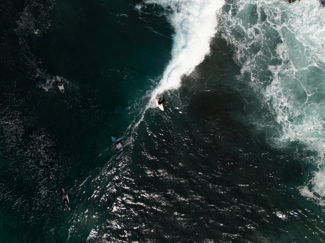 Aerial view of surfers riding waves in the deep blue ocean with white foam and clear water in Dee Why New South Wales Australia.