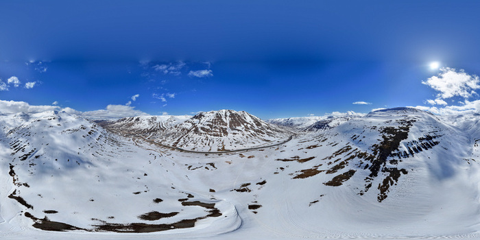 Aerial view of snow covered mountain peaks and a winding road under a clear blue sky in the arctic landscape Horgarsveit Iceland.