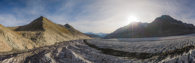 Aerial view of the Aletsch Glacier with rugged mountain peaks deep ice crevasses and sun flare over the landscape in Fieschertal Valais Switzerland. Aerial view of the Aletsch Glacier with rugged mountain peaks deep ice crevasses and sun flare over the landscape in Fieschertal Valais Switzerland.