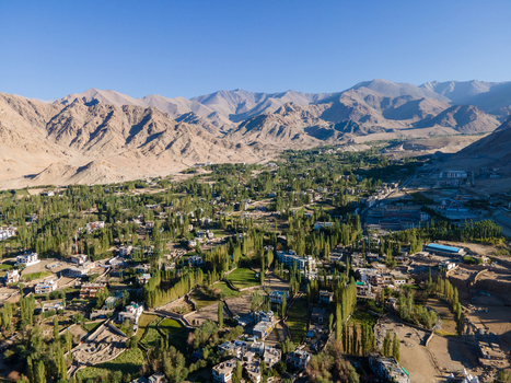 Aerial view of a lush green valley with scattered houses and trees nestled among arid rugged mountain ranges under a clear blue sky in Ladakh Division Ladakh India. Aerial view of a lush green valley with scattered houses and trees nestled among arid rugged mountain ranges under a clear blue sky in Ladakh Division Ladakh India.
