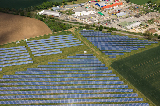 Aerial view of rows of solar panels on a green field next to industrial buildings and agricultural land Sivice South Moravian Region Czechia.
