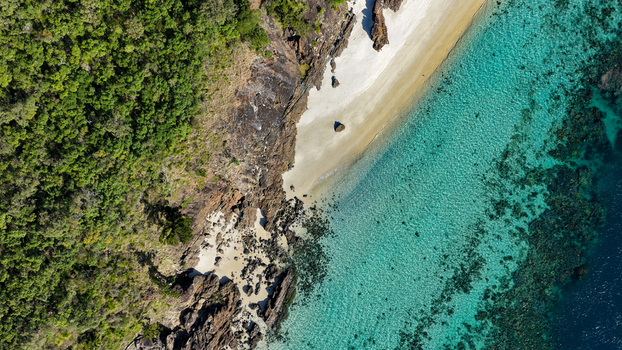 Aerial view of the pristine white sand beach and turquoise waters of Haslewood Island surrounded by lush green vegetation and rocky cliffs in Whitsundays Queensland Australia. Aerial view of the pristine white sand beach and turquoise waters of Haslewood Island surrounded by lush green vegetation and rocky cliffs in Whitsundays Queensland Australia.