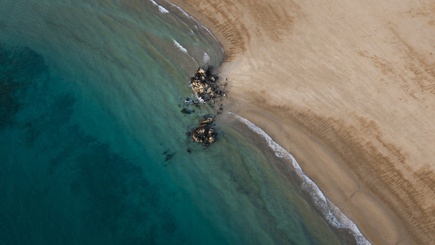 Aerial view of the coastline with turquoise ocean waves meeting golden sand and dark rock formations in Plevenon Brittany France. Aerial view of the coastline with turquoise ocean waves meeting golden sand and dark rock formations in Plevenon Brittany France.