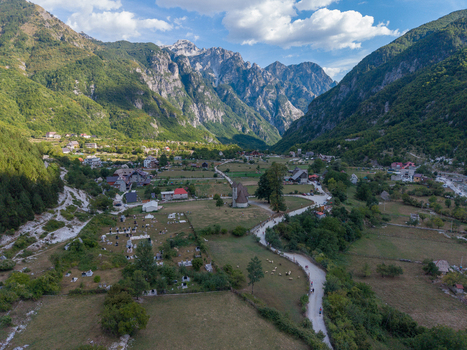 Aerial view of the historic Church of Theth in the lush valley of the Albanian Alps surrounded by dramatic mountain peaks winding roads and stone houses in Theth Shkoder County Albania. Aerial view of the historic Church of Theth in the lush valley of the Albanian Alps surrounded by dramatic mountain peaks winding roads and stone houses in Theth Shkoder County Albania.