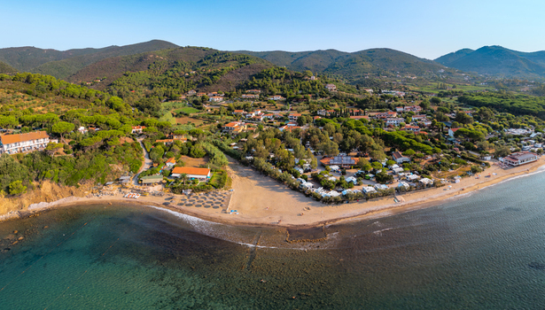 Aerial view of Lacona Beach with its sandy shoreline surrounding Mediterranean vegetation and nearby camping facilities nestled against the hills in Lacona Tuscany Italy.