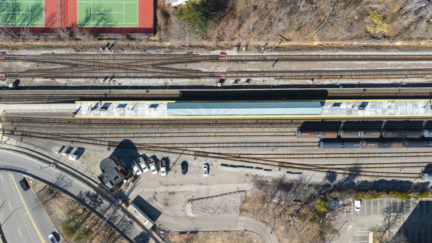 Aerial view of railway tracks cutting through the landscape leading to a station platform amidst a parking lot and tennis court Braintree Massachusetts United States.