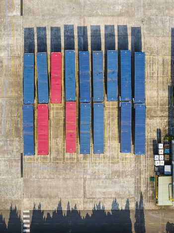 Aerial view of rows of blue and red shipping containers arranged in a concrete yard with long shadows cast by the afternoon sun in Taiwan. Aerial view of rows of blue and red shipping containers arranged in a concrete yard with long shadows cast by the afternoon sun in Taiwan.