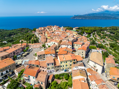 Aerial view of the historic town of Capoliveri with its dense terracotta rooftops narrow streets and lush surrounding landscape overlooking the blue sea in Capoliveri Tuscany Italy.