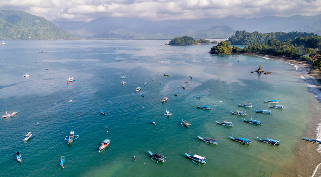 Aerial view of Prigi Beach with numerous small fishing boats scattered across the turquoise water mountains in the background clear sky calm sea in Kecamatan Watulimo Jawa Timur Indonesia. Aerial view of Prigi Beach with numerous small fishing boats scattered across the turquoise water mountains in the background clear sky calm sea in Kecamatan Watulimo Jawa Timur Indonesia.